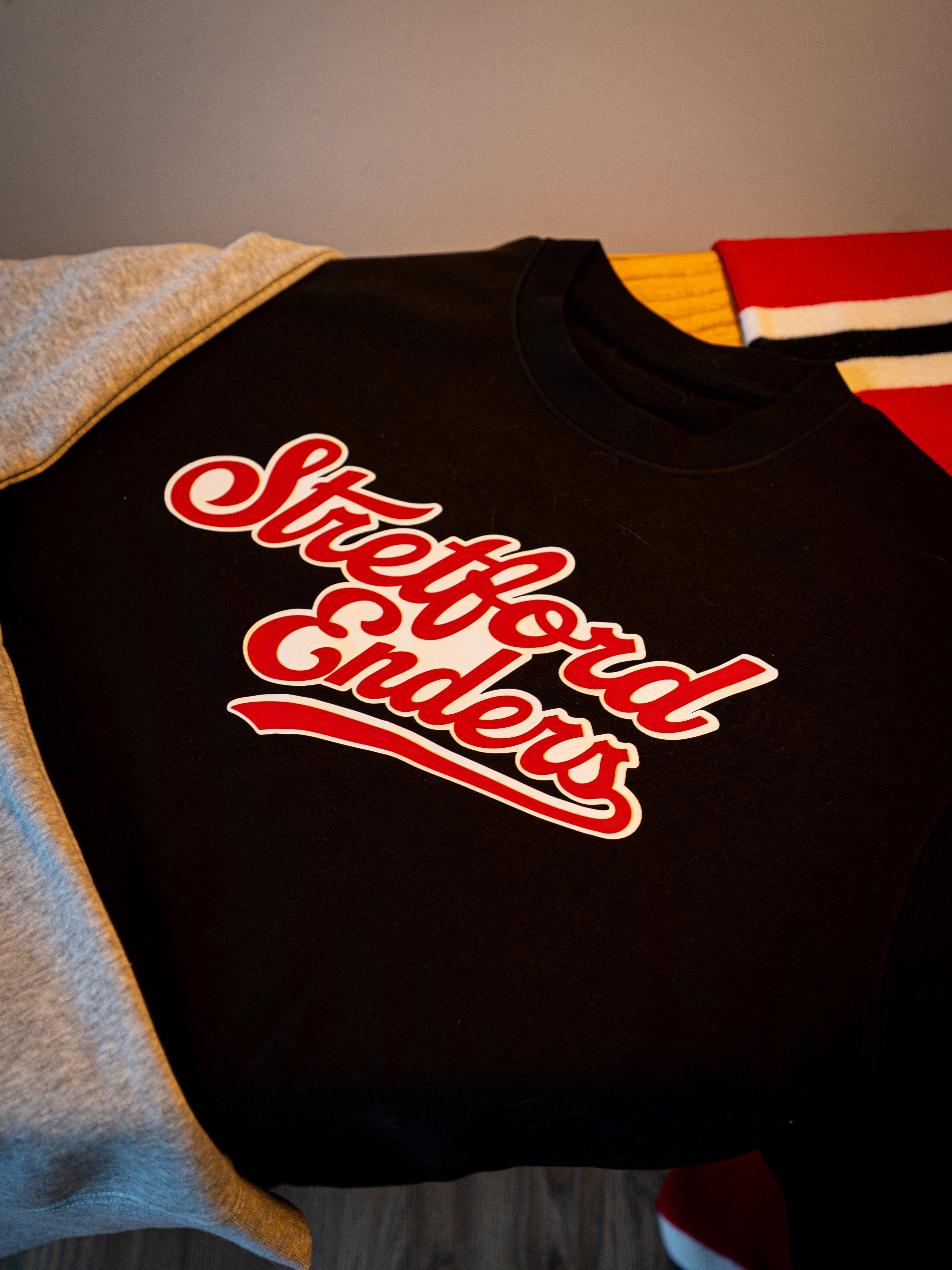 Black sweatshirt with red text 'Stretford Enders' on a neutral background